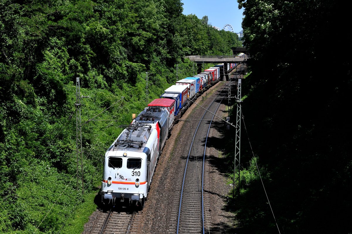Am 30. Juni 2019 wurde von Kombiverkehr anläßlich des 50-jährigen Firmenjubiläums eine schöne Aktion ins Leben gerufen. Als Sonderleistung wurde ein DGS 69050 von München Ost Rangierbahnhof nach Frankfurt Main (Ost) UBF eingelgt. Dabei handelte es sich um einen 540 Meter langen Zug, der mit 35 verschiedenen Sattelaufliegern, Tankcontainern und Wechselbehältern der besten Kunden von Kombiverkehr beladen war. Passend bespannt wurde dieser von der extra für diesen Anlass in einem Jubiläumsdesign gestalteten 139 135. Dahinter lief die ohnehin im Kombiverkehr-Design gehaltene 185 665 kalt mit. Der Zug wurde auf seinem Laufweg naturgemäß von vielen Fotografen und Trainspottern erwartet. Eines der ersten Bilder der gelungenen Aktion konnte ich am Einschnitt am Nockherberg in München anfertigen. Ein inzwischen historisches kurioses Detail am Rande war die Beschriftung der 139 135 an diesem Tage. Im Vorfeld kam es zu einem Mißverständnis mit dem Modelleisenbahnhersteller Piko, welcher ein Modell der Lok als 139 310 auf den Markt bringen möchte. Als Lösung wurde die 139 135 kurzerhand an Front und Seite mit einer großen  310  versehen... 