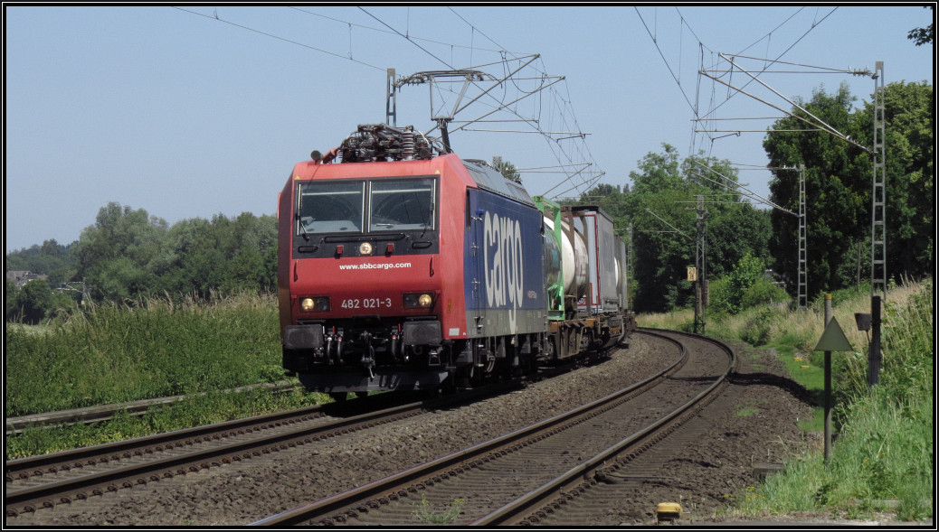 Am 30.Juni 2015 kommt die 482 021-3 der SBB Cargo als Umleiter mit ihrer Güterfracht in den Gleisbogen bei Rimburg gefahren. Hier zu sehen am BÜ auf der Kbs 485.