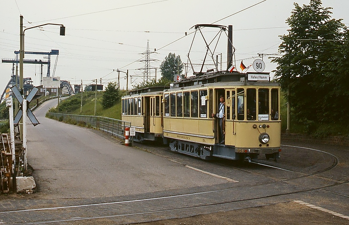 Am 31.05.1986 verlassen der Museums-Tw 954 und der passende Bw 858 das Endgleis in Düsseldorf Hamm. Die Straße führt zu der im Hintergrund sichtbaren Baustelle der neuen Eisenbahnbrücke über den Rhein.