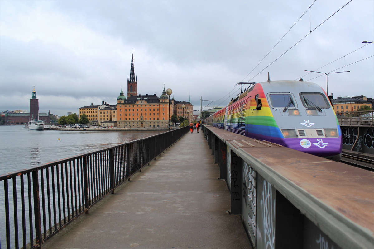 Am 31.08.2018 verlässt Snabbtåg 427 nach Göteborg die schwedische Hauptstadt Stockholm über die beiden Brücken über den Mälarsee. Der eingesetzte X2 erhielt anlässlich der diesjährigen Euro Pride eine auffällige Sonderbeklebung. Es waren die letzten Einsatztage dieses Zuges in dem Gewand, das schon etwas gelitten hat.