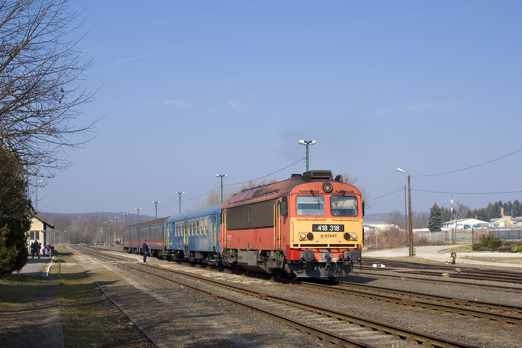 Am 4. März 2022 ist 418 318 mit Sz 39514 unterwegs und verlässt nach erteilter Abfahrtserlaubnis durch den örtlichen Fahrdienstleiter den Bahnhof Zirc in Richtung Veszprem. 