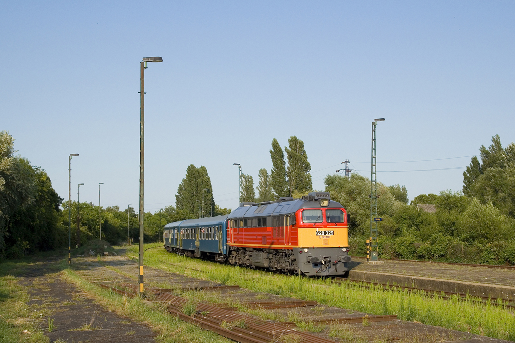 Am 9. Juli 2023 ist 628 329 mit dem Sz 19786 (Balatonfüred - Tapolca) unterwegs. Soeben erreicht der Zug den Bahnhof Révfülöp und wird einen rund zehnminütigen Kreuzungsaufenthalt aufgrund eines verspäteten Gegenzuges einlegen. 