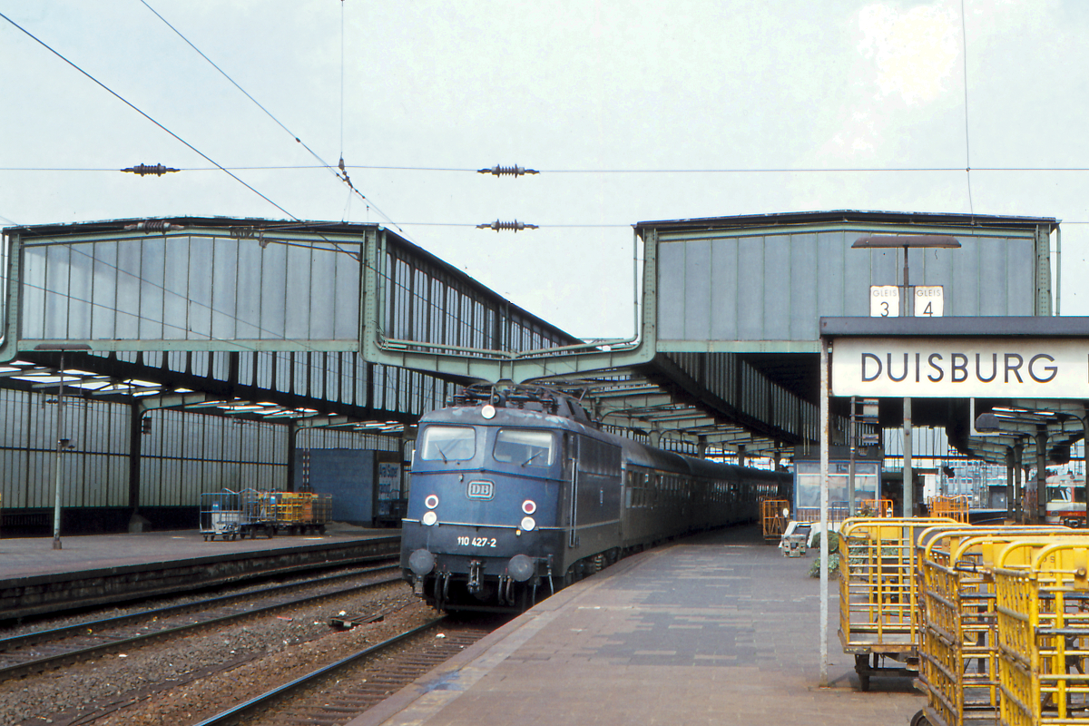 Am 9. September 1978 steht die 110 427 mit dem Eilzug Cuxhaven - Münster - Aachen abfahrbereit in Duisburg Hbf. Der Zug bestand aus für 140 km/h zugelassenen Silberlingen und konnte so im Norddeutschen Flachland ziemlich forsch fahren. Im Jahr 1978 bot die damalige Deutsche Bundesbahn für Jugendliche das  Tramper-Monatsticket  an. Ich nutzte es, um Deutschland zu erkunden.
Mir persönlich gefällt das Foto, auch weil ich seither nicht wieder nach Westfalen gelangt bin. Der erste Scan des Fotos lieferte noch unbefriedigende Ergebnisse. Erst mit einem neuen Scanner gelang ein  vorzeigbares  Ergebnis.
Duisburg Hbf, 9.9.1978