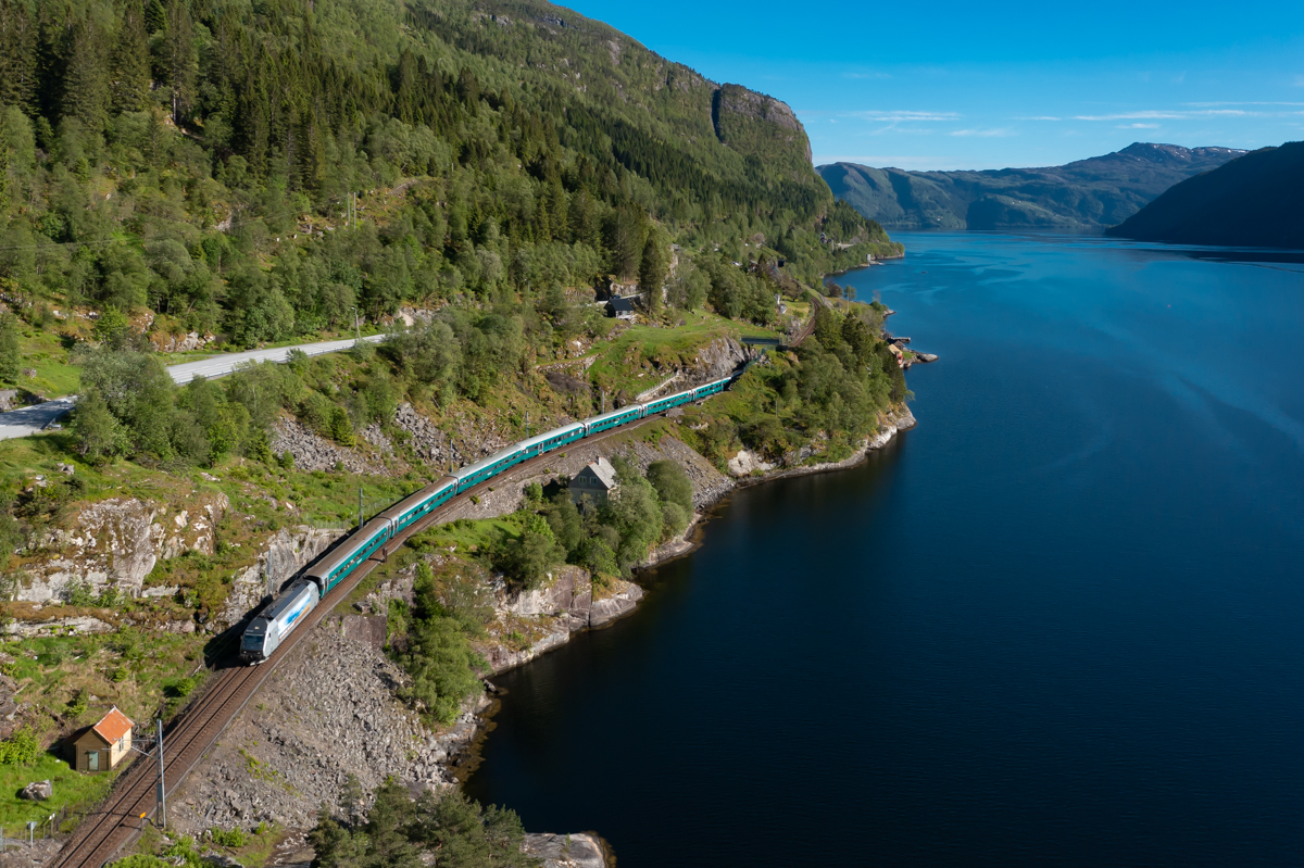 Am Abend des 05.06.2022 ist Reg 66 von Bergen in Richtung Oslo unterwegs. Die ersten Kilometer verlaufen dabei an der Küste des Veafjordes nordöstlich von Bergen. Die Fahrgäste können dabei den Blick auf die beeindruckende norwegische Landschaft genießen. In wenigen Minuten wird der Zug den Bahnhof Stanghelle durchfahren.