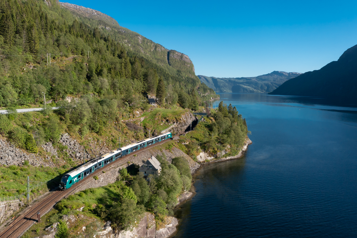 Am Abend des 06.06.2022 ist Zug 1826 von Bergen in Richtung Voss unterwegs. Die Fahrgäste genießen derweil den Blick auf den Veafjord, an dessen Ufer die Bahn bis Stanghelle verläuft. In kürze wird Stanghelle erreicht.