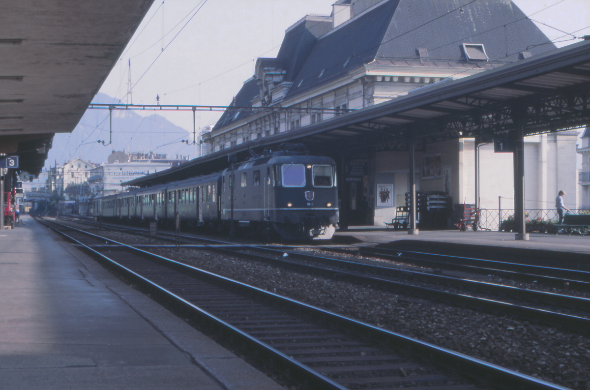 Am Abend des 22.August 1987 ist die Re 4/4 II der SBB mit einem Regionalzug aus Lausanne in Montreux angekommen. Der Zug hatte dort ein paar Minuten Aufenthalt, um die Überholung durch einen anderen Zug abzuwarten - so bleib mir genügend Zeit, den Zug, mit dem ich gerade angekommen war, im Bild festzuhalten. Der Zug erscheint geradezu klein neben dem imposanten Empfangsgebäude.
Montreux, 22.08.1987; Canon AE-1, Canoscan, Gimp