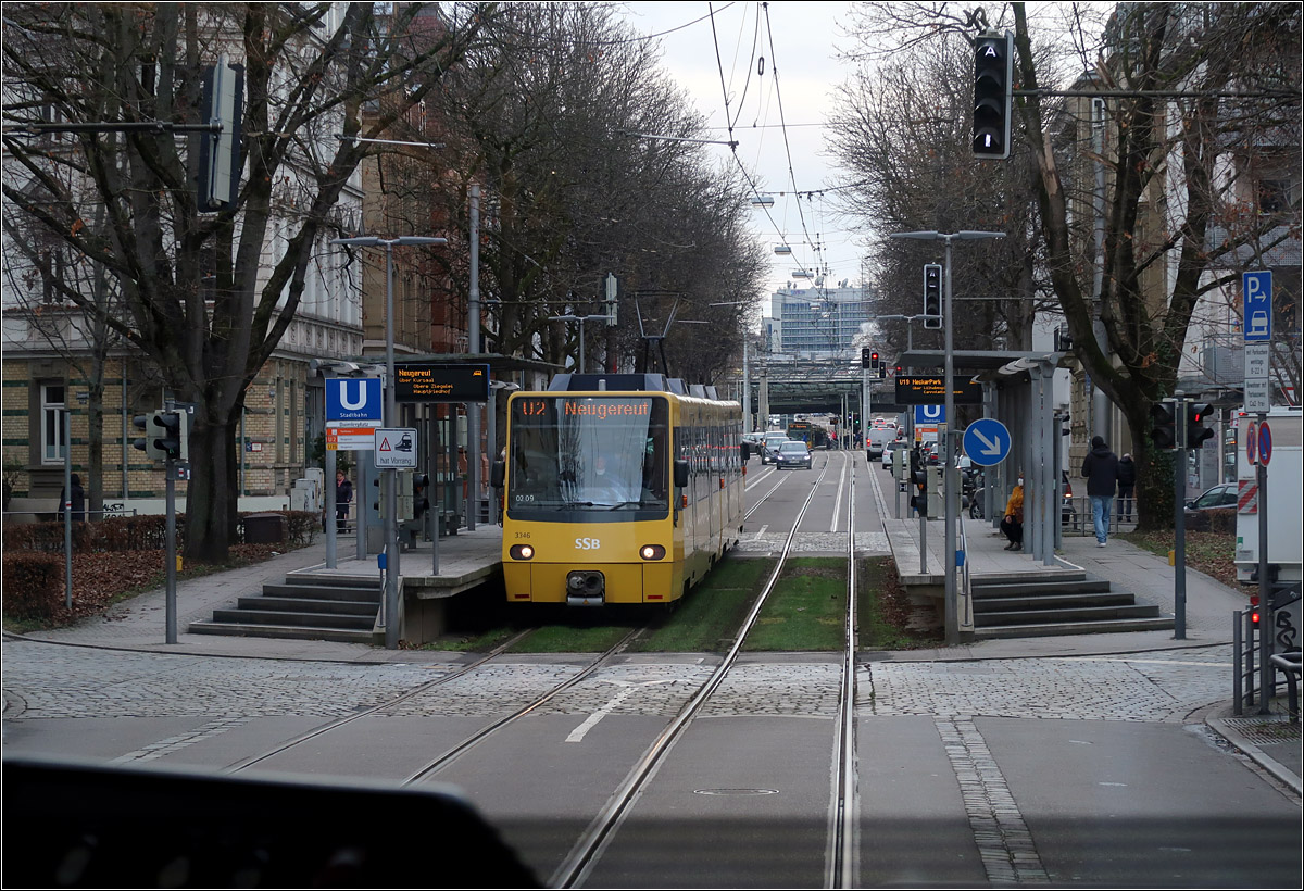 Am Daimlerplatz -

.. in Bad Cannstatt befindet sich die Stadtbahnhaltestelle der Linien U2 und U19 inmitten eines Kreisverkehrs. Rampen und Stufen führen auf die etwas abgesenkten Hochbahnsteige, was auch am Verlauf der Schienen erkennbar ist, die im Haltestellenbereich etwas tiefer liegen, als auf den Straßenabschnitten davor und dahinter. 
Weiter hinten ist in der Haltestelle Wilhelmsplatz ein weiterer Stadtbahnzug erkennbar, vermutlich auf der Linie U1. Ganz in der Flucht der Straße ist ein SWR-Gebäude erkennbar.

Aufnahmestandpunkt im Fahrgastraum einer Stadtbahn.

03.02.20202
