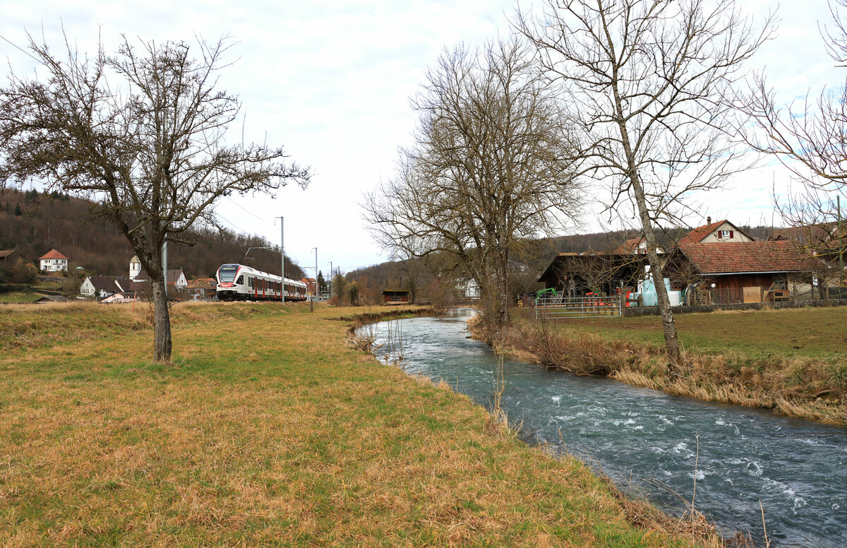 Am Fluss Allaine, mit Blick auf die kleine jurassische Ortschaft Buix in der Ajoie. Gerade fährt der mittägliche Schülerzug nach Boncourt durch (Flirt 523 034). 18.Februar 2022 