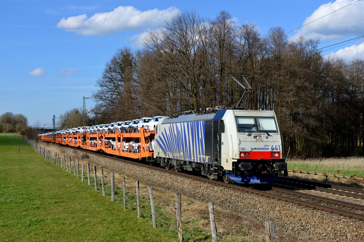 Am Karfreitag, den 03. April 2015, waren erstaunlich viele Güterzüge auf der KBS 950 unterwegs. So auch der DGS 48867 von München Nord nach Oberitalien, der stets Neuwagen aus dem VW-Konzern geladen hat. Zuglok war die 186 441, aufgenommen wurde die Leistung am Bahnübergang bei Vogl.  Arger Rollo-Schaden , wie ein Anhänger der  Wiener Schule  wohl bemängeln würde, aber das gehört zum Bahnbetrieb nunmal dazu und tut dem farbenfrohen Gespann keinen Abbruch.