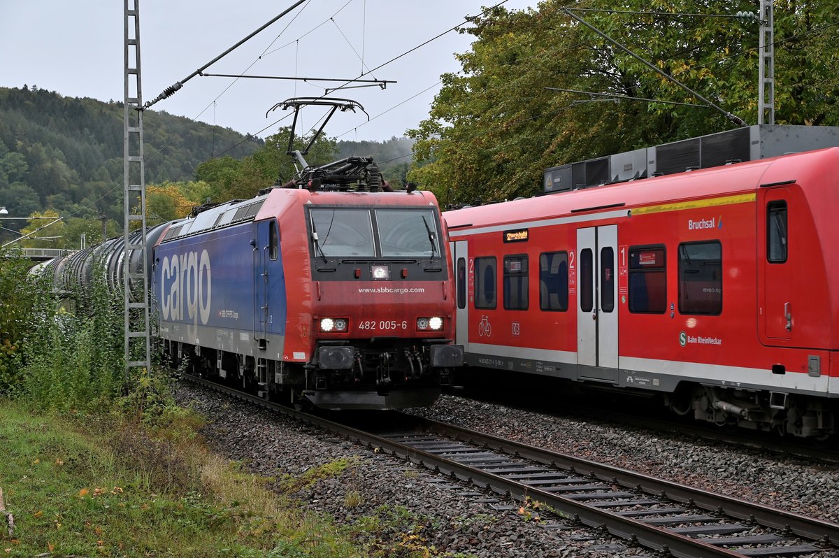 Am Mittag des 6. Oktober 2020 ist die SBB Cargo 482 005 mit einem Öler gen Mosbach- Neckarelz durch Neckargerach abgelichtet, auf dem Nebengleis ist der 425 namens Bruchsal bei der Anfahrt an den Bahnsteig in Neckargerach mit aufs Bild geraten.