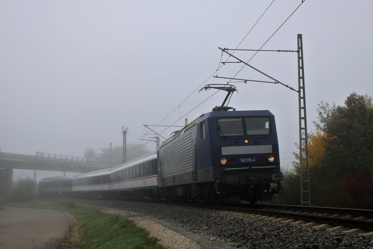 Am Morgen des 04.10.2022 schiebt sich 143 295-4 der Weser-Ems-Eisenbahn mit ihrem Ersatzzug auf der RS21 nach Ulm Hbf durch den noch dichten Nebel. Hier ist der Zug gerade in der Verbindungskurve in Laupheim West zu sehen.