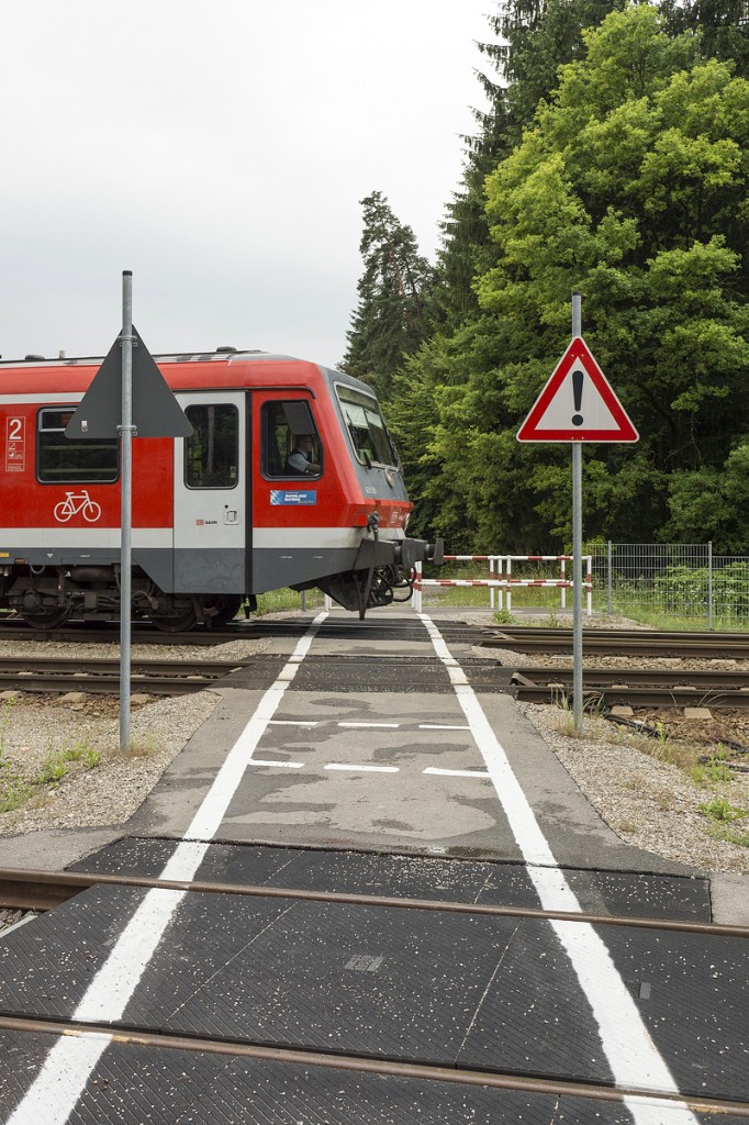 Am Nordkopf des Bahnhofs Kastl (Oberbayern) befindet sich ein Fußgängerbahnübergang. Im Vordergrund verläuft das Ausziehgleis der Wüst des Industrieparks Burgkirchen a.d. Alz. Dahinter folgt mit einigem Abstand das Güterzugausweichgleis, an dem auch die Wüst angeschlossen ist. Dahinter befindet sich das durchgehende Hauptgleis der Relation Burghausen - Mühldorf und das Ausweichgleis für Reisezüge in Richtung Burghausen. Der Bahnübergang befindet sich im Weichenbereich der beiden letztgenannten Gleise zwischen Weichenzungen und Herzstück.
Zwischen dem Ausziehgleis und dem Güterzugausweichgleis befindet sich zwischen den gestrichelten Querlinien ein sicherer Bereich, in dem auf eine Größe von etwas mehr als 1qm Passanten Zugfahrten abwarten können. Dieser Bereich ist beidseitig durch ein Gefahrenzeichen nach StVO gesichert.
Auf dem durchgehenden Hauptgleis fährt 628 559 nach Mühldorf aus.
20.06.2014