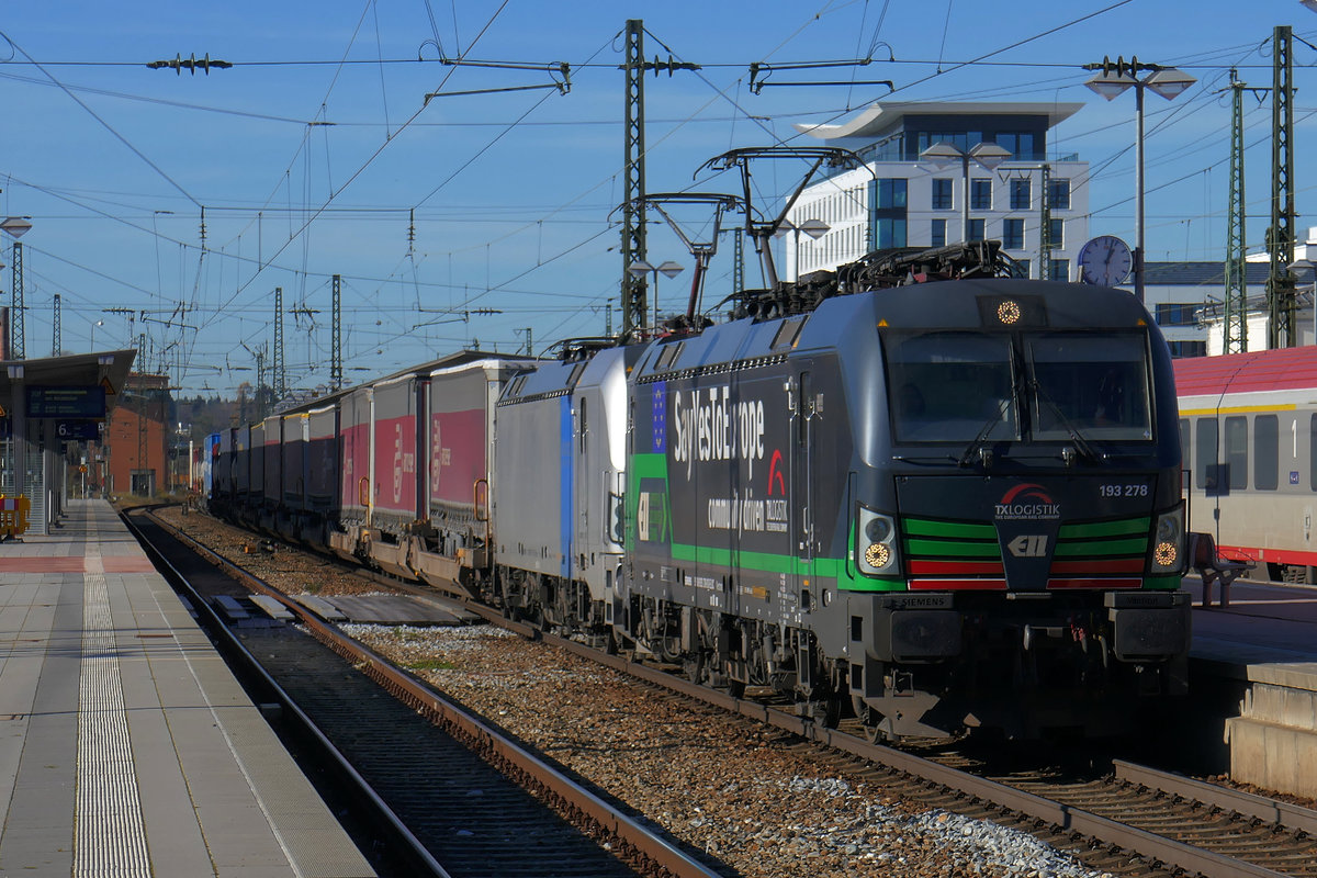 Am sonnigen 21. November 2020 durchfahren zwei Vectron mit einem Zug des kombinierten Ladungsverkehrs den Bahnhof Rosenheim auf Gleis 5. Es führt 193 278  Say Yes To Europe  von ELL, vermietet an TXL; dahinter ist 193 991 von Railpool eingereiht. Auf dem Nachbargleis steht ein Eurocity nach Klagenfurt.