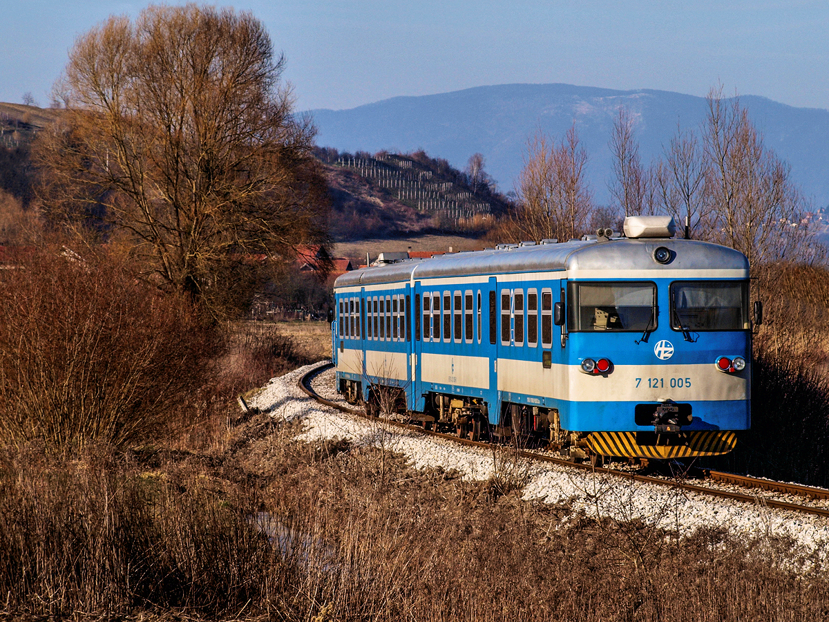 Am sonnigen und frischen Nachmittag des 20.02.2015. fährt er Triebwagen 7121 005 gerade als Regionalzug 3130 von Zabok nach Djurmanec durch die Felder und Sümpfe nördlich der Stadt Zabok. In Kürze seinen nächsten Zwischenhalt, die Haltestelle von Strucljevo erreichen. Die Sonne steht bereits ziemlich niedrig und in wenigen Minuten wird schon der Schatten der nahe gelegenen Hügel die Gleise erreichen.