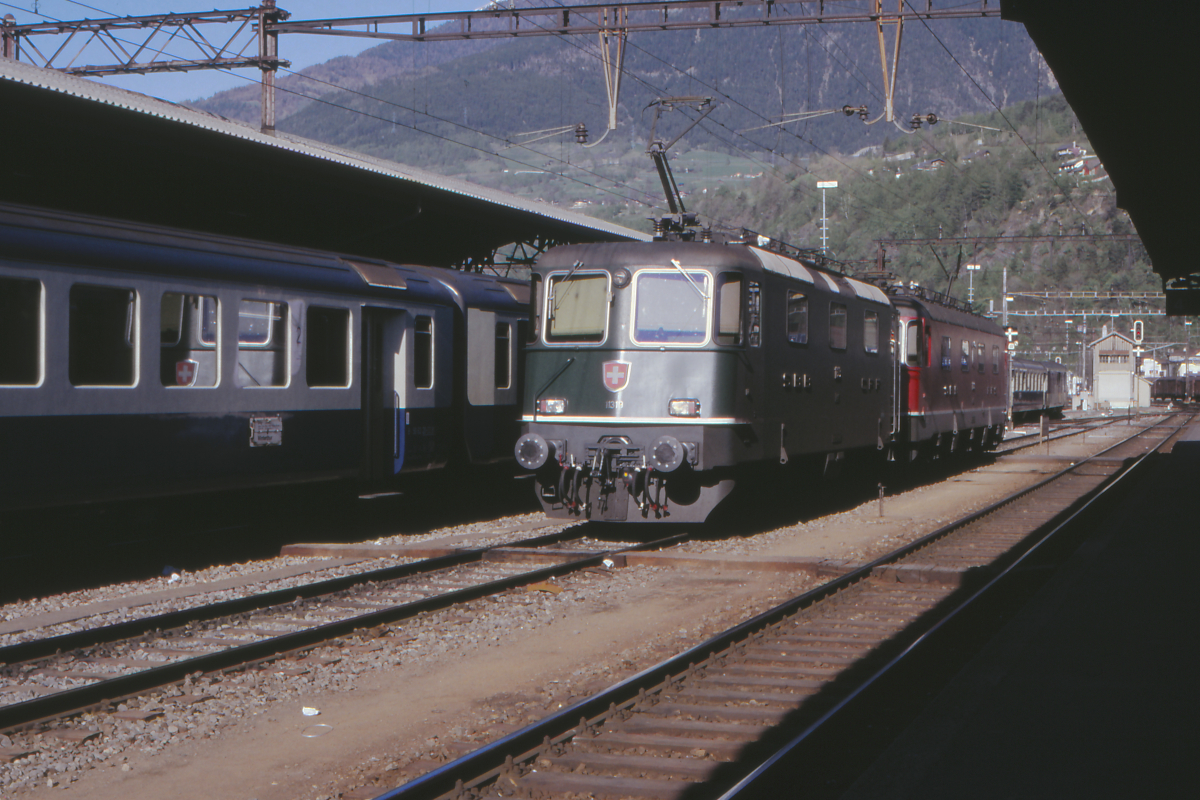 Am späten Nachmittag des 28. April 1990 warten die Re 4/4 II 11319 und eine unbekannte Re 6/6 der SBB in Brig auf ihren nächsten Einsatz. Die Re 4/4 II hat schon eckige Lampen und Haltegriffe für Rangierer, ist aber noch im traditionellen  SBB-Grün  lackiert. Am Nachbargleis steht ein Zug mit Einheitswagen II der BLS-Gruppe mit dem Zuglaufschild Brig - Winterthur - die Fahrt ging damals natürlich über den Lötschberg, der Basistunnel war noch  Zukunftsmusik . 
Brig, 28.April 1990; Canon A1, Canoscan, Gimp