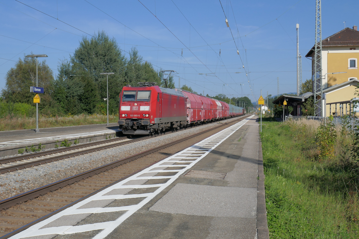 Am späten Nachmittag des Dienstags, 14. September 2021, durchfährt 185 065 den Bahnhof Übersee auf ihrem Weg von Freilassing nach Rosenheim. Am Haken hat sie den  Müllzug : Er wurde mit Diesellok 077 018 von Burgkirchen nach Freilassing gebracht, wo ihn die 185 065 übernahm. Ein Teil des Zuges ist mit Müllcontainern für die Ladestelle Thansau bei Rosenheim beladen.