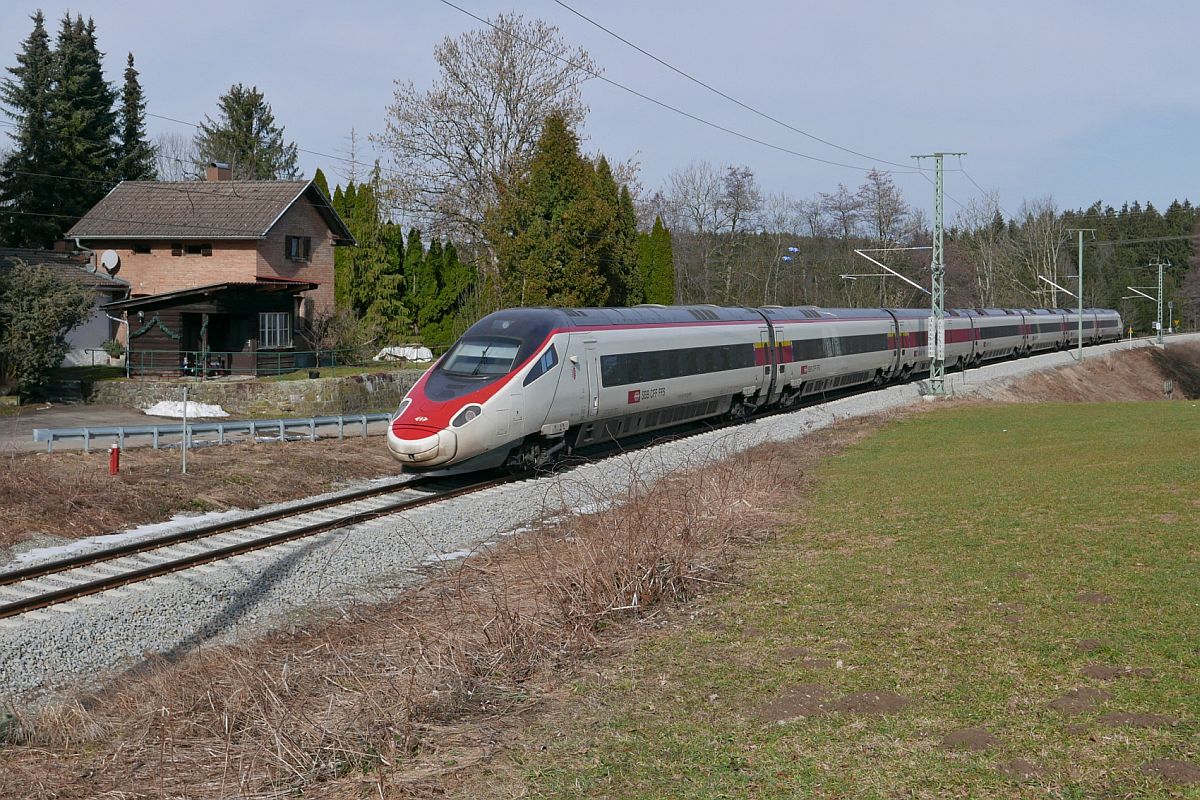 An einem ehemaligen Schrankenw�rterh�uschen in der N�he von Hergatz befindet sich am 22.02.2021 RABe 503 013  Valais / Wallis  als ECE 99 auf der Fahrt von Z�rich nach M�nchen.