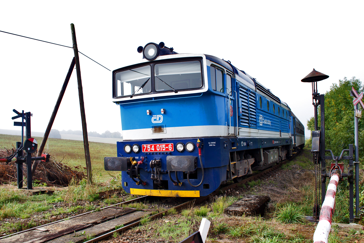 An einem historischen Bahnübergang in Nyrsko dieselt die 754 015-6 am Morgen des 12.9.2015 mit dem Schnellzug 775 vorüber.