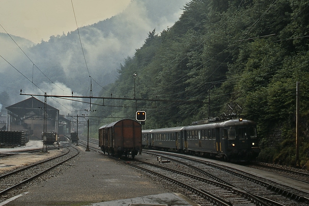An einem völlig verregneten Julitag 1983 kommt ein RBe 4/4 der SBB auf seiner Fahrt von Moutier nach Delemont im inzwischen stillgelegten Bahnhof Choindez an. Im Hintergrund sind die Hallen des von Roll-Werkes und die damals noch eingesetzte E 2/2 9 sichtbar.