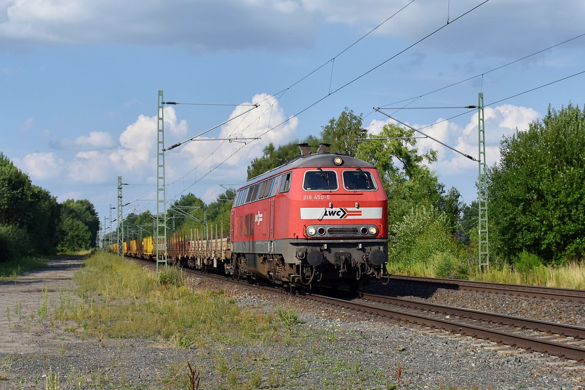 An einem der wenigen Tage, an denen sich im Sommer 2018 auch mal Wolken zeigten, dieselte die 218 450 von LWC mit einem langen Bauzug aus Rungenwagen durch den Haltepunkt Westbevern in Richtung Münster. Sie trägt noch das (ausgeblichene) verkehrsrote Farbkleid der DB.