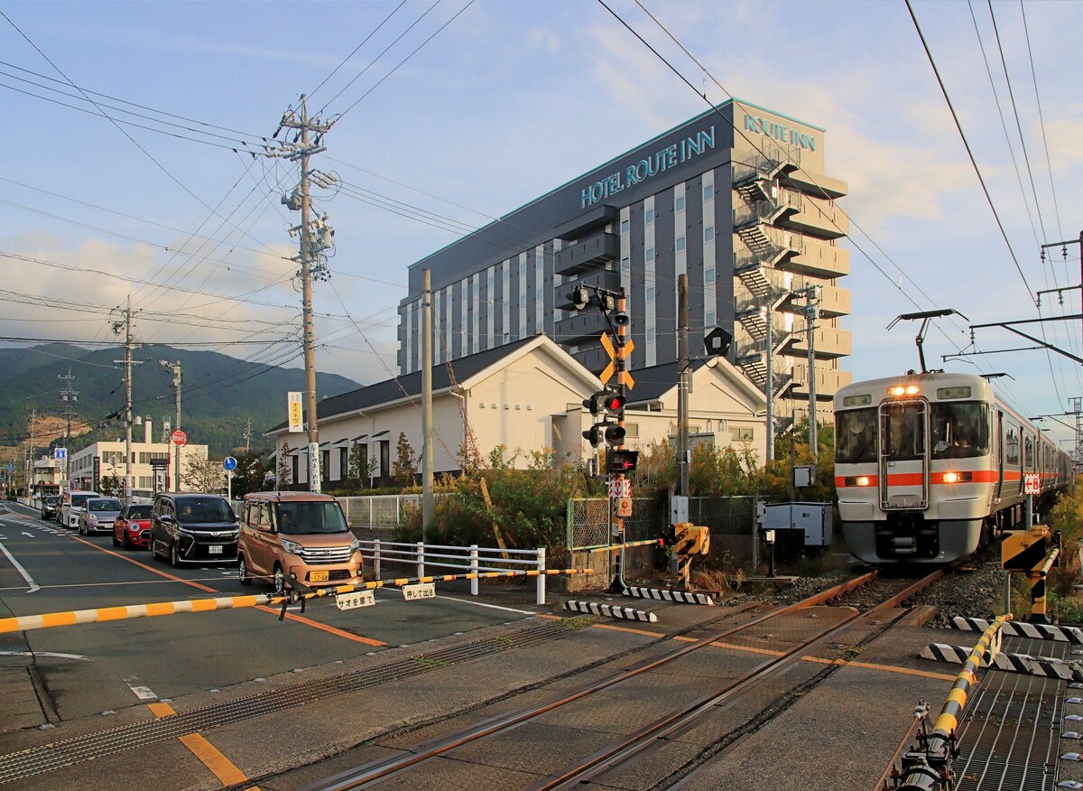 An der Iida Linie in Zentraljapan: Zwei Zweiwagenzüge (313-3021 + 313-3023) in der Morgenspitze erreichen die kleine Ortschaft Shinshiro. Es ist immer wieder erstaunlich, welch riesige Hotels an solchen Orten entstehen, günstig, sauber und voller Annehmlichkeiten. 6.November 2023 