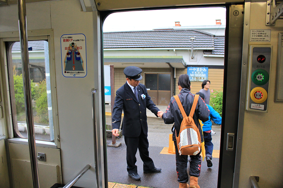 An der Strecke von Tokushima ins Innere der Insel Shikoku. Links von der Türe prangt ein Bild, wie man den Zug bei Einmannbetrieb benutzen soll. Hinten einsteigen und einen Zettel mit Kontrollnummer nehmen, beim Aussteigen wartet der Wagenführer hinter dem Geldkasten, in den man den der Kontrollnummer entsprechenden Betrag einwirft. Doch heute zieht es der Fahrer vor, die Beine zu strecken und draussen im Freien die Kontrolle durchzuführen. Aus Triebwagen 1251, in Awa-Yamakawa, 3.April 2015.   