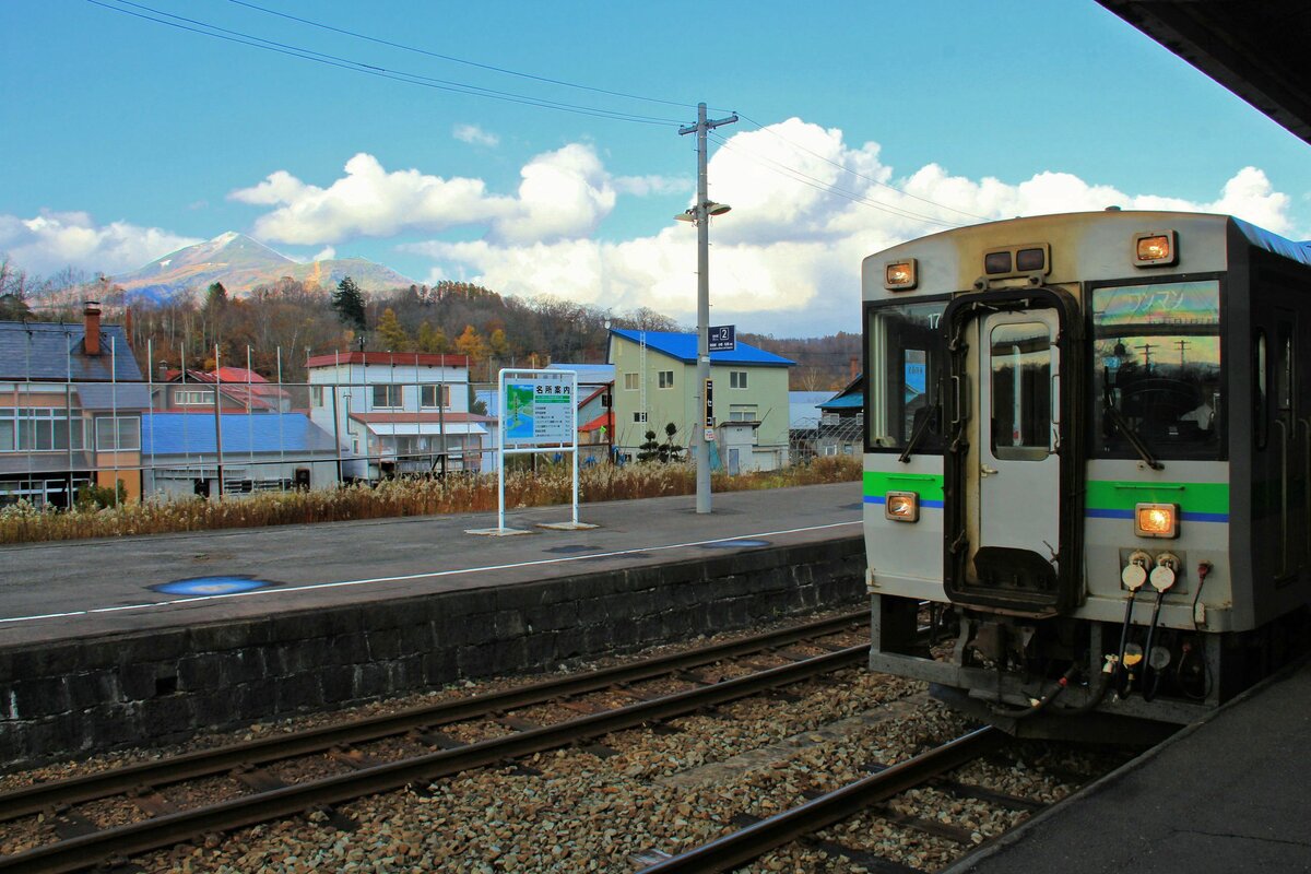 An der Südseite der alten Hauptstrecke von Hakodate nach Sapporo über den Pass von Oshamambe nach Otaru: KIHA 150-17 hält kurz in Niseko, mit Blick auf die Niseko-Annupuri Berge. Hier herrscht im Winter viel Betrieb mit Wintersport. 29.Oktober 2015 