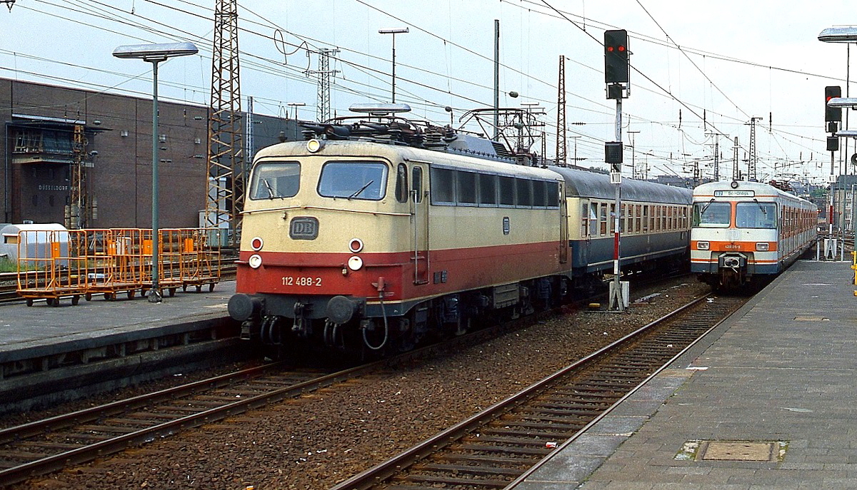 Anfang der 1980er Jahre fahren 112 488-2 mit einem D-Zug und ein 420 als S 7 nach Solingen-Ohligs in den Düsseldorfer Hauptbahnhof ein