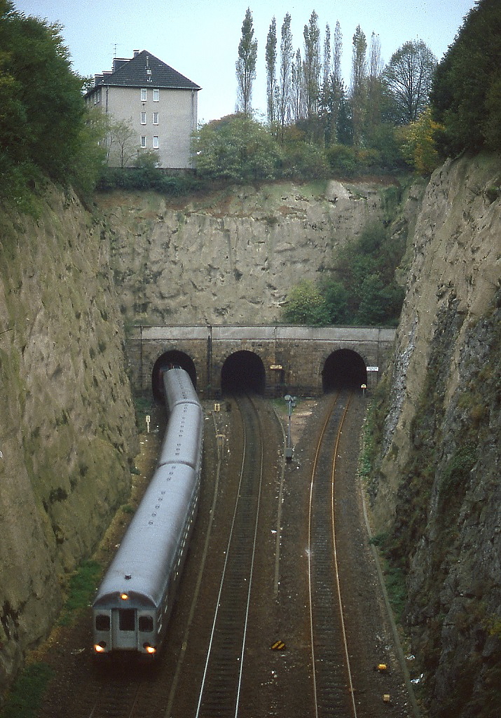 Anfang der 1980er Jahre schiebt eine 212 einen Nahverkehrszug mit einem führenden Steuerwagen vom Typ BDnf238 durch den Rauenthaler Tunnel in Wuppertal. Das rechte Gleis führte durch den Langerfelder Tunnel zum inzwischen geschlossenen Containerbahnhof in Wuppertal-Langerfeld.
