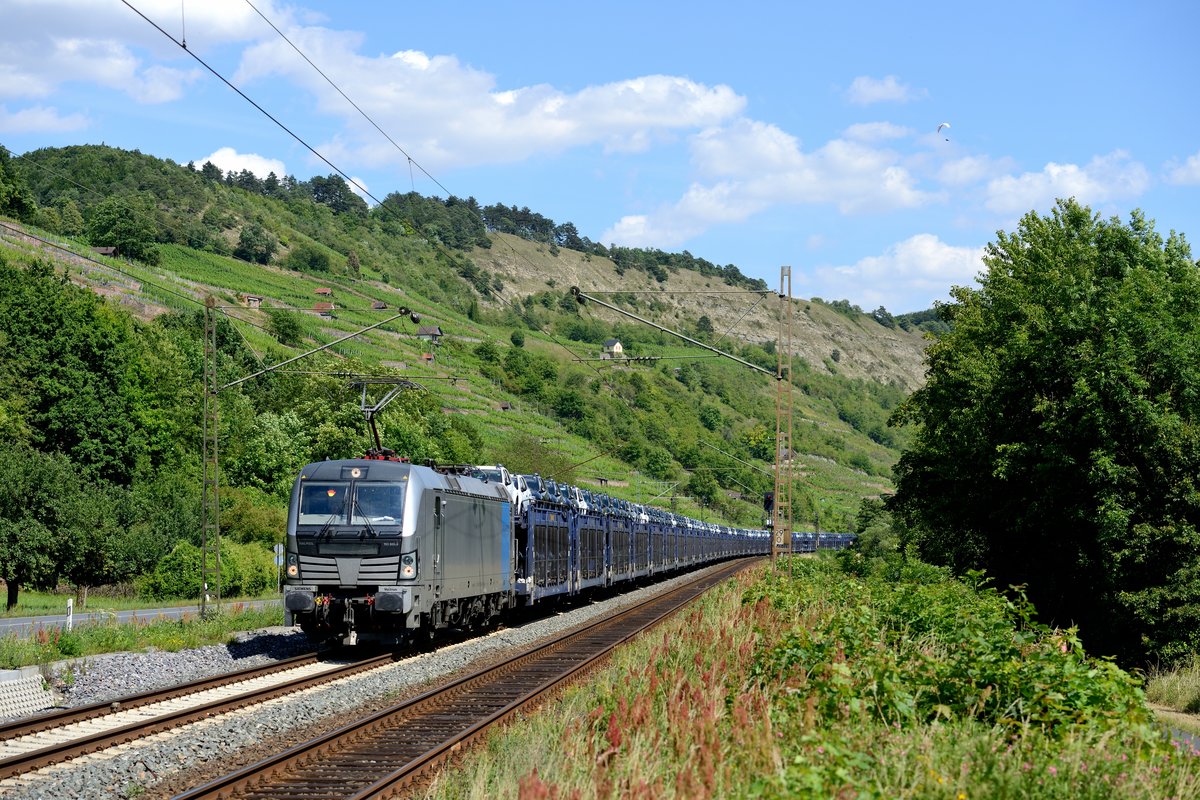 Anlässlich der WM hat der Tf den Führerstand seines Railpool-Vectrons 193 805 entsprechend dekoriert. Am Haken ein Autotransportzug aus Rumänien, beladen mit Neuwagen des Herstellers Dacia. Bei Gambach wollte am 03. Juli 2014 auch noch ein Paraglider mit auf's Bild....