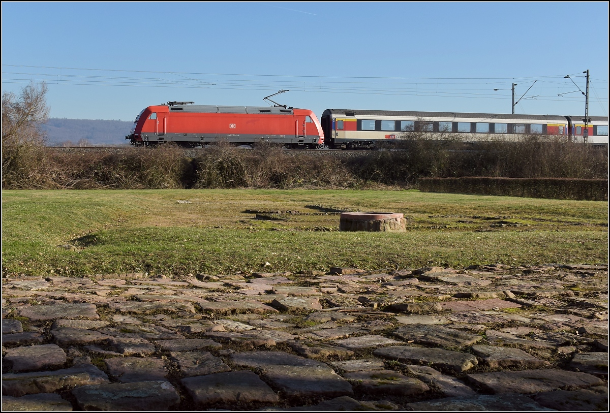 Antike und heute. Die badische Hauptbahn folgt in weiten Bereichen den alten Römerstraßen. Hier in Friesenheim wird ein Stück Römerstraße mit Raststätte an einer antiken Kreuzung gepflegt, netterweise direkt neben der Bahnstrecke. 101 115 mit einem EC auf Römerpfaden. Februar 2019.