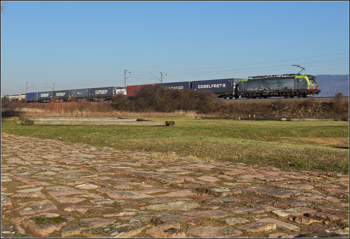 Antike und heute. Die badische Hauptbahn folgt in weiten Bereichen den alten Römerstraßen. Hier in Friesenheim wird ein Stück Römerstraße mit Raststätte an einer antiken Kreuzung gepflegt, netterweise direkt neben der Bahnstrecke. Re 475 405 mit einem Güterzug auf Römerpfaden. Februar 2019.