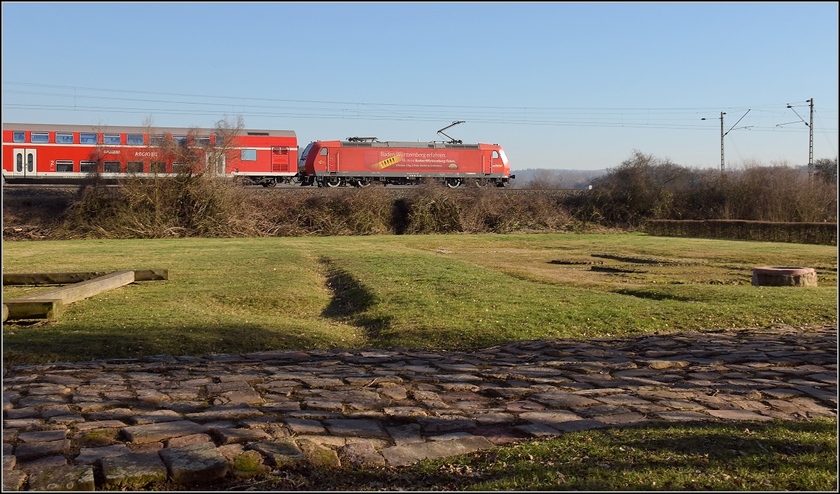 Antike und heute. Die badische Hauptbahn folgt in weiten Bereichen den alten Römerstraßen. Hier in Friesenheim wird ein Stück Römerstraße mit Raststätte an einer antiken Kreuzung gepflegt, netterweise direkt neben der Bahnstrecke. 146 115 mit einem RE auf Römerpfaden. Februar 2019.