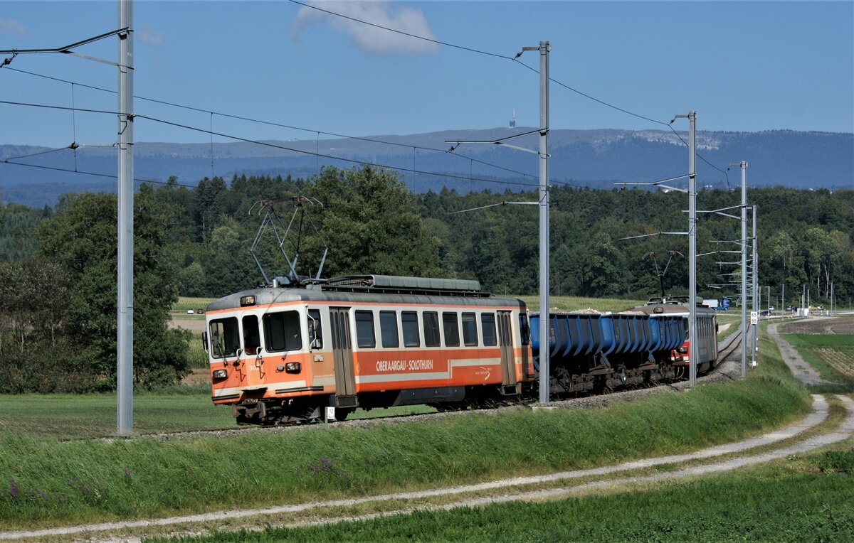 ASM BTI Aare Seeland mobil AG Biel-Täuffelen-Ins-Bahn: Be 4/4 302 + Fa 572 + Fa 571 + Fa 576 + Be 4/4 304, Zug 8250 Sutz-Finsterhennen, Lüscherzmoos (km 12,4), 1. September 2021. Am rechten Bildrand ist der Parkplatz an der Haltestelle Lüscherz und der Beginn des Bahnsteiges zu erkennen. Das Dorf Lüscherz selbst liegt hinter dem Wald am Bielersee. Den Horizont bildet der Chasseral mit Fernmeldeanlage und Berghotel. 