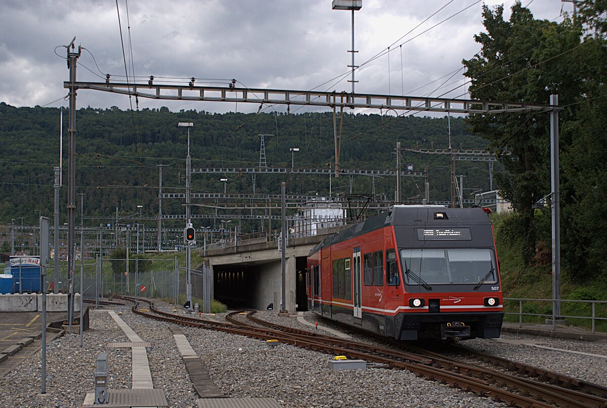 ASm BTI Aare Seeland mobil AG Biel-Täuffelen-Ins-Bahn: GTW 507 + 504, Zug 8116 Biel-Täuffelen, Biel, 23. Juli 2025. Die Ausweiche im Tunneleingang wird im normalen Fahrplanbetrieb nicht für Kreuzungen benötigt. Hier befanden sich einst die Güteranlagen der BTI mit zwei Rollschemelgruben im umzäunten Gleisbereich im Bildhintergrund (inzwischen stark zurückgebaut). Innerhalb der Umzäunung steht der stationäre  WR   Soup-y-Rail  (ex B MOB/TPF) der kirchlichen Gassenarbeit Biel (zuvor in ähnlicher Verwendung in Bulle). 