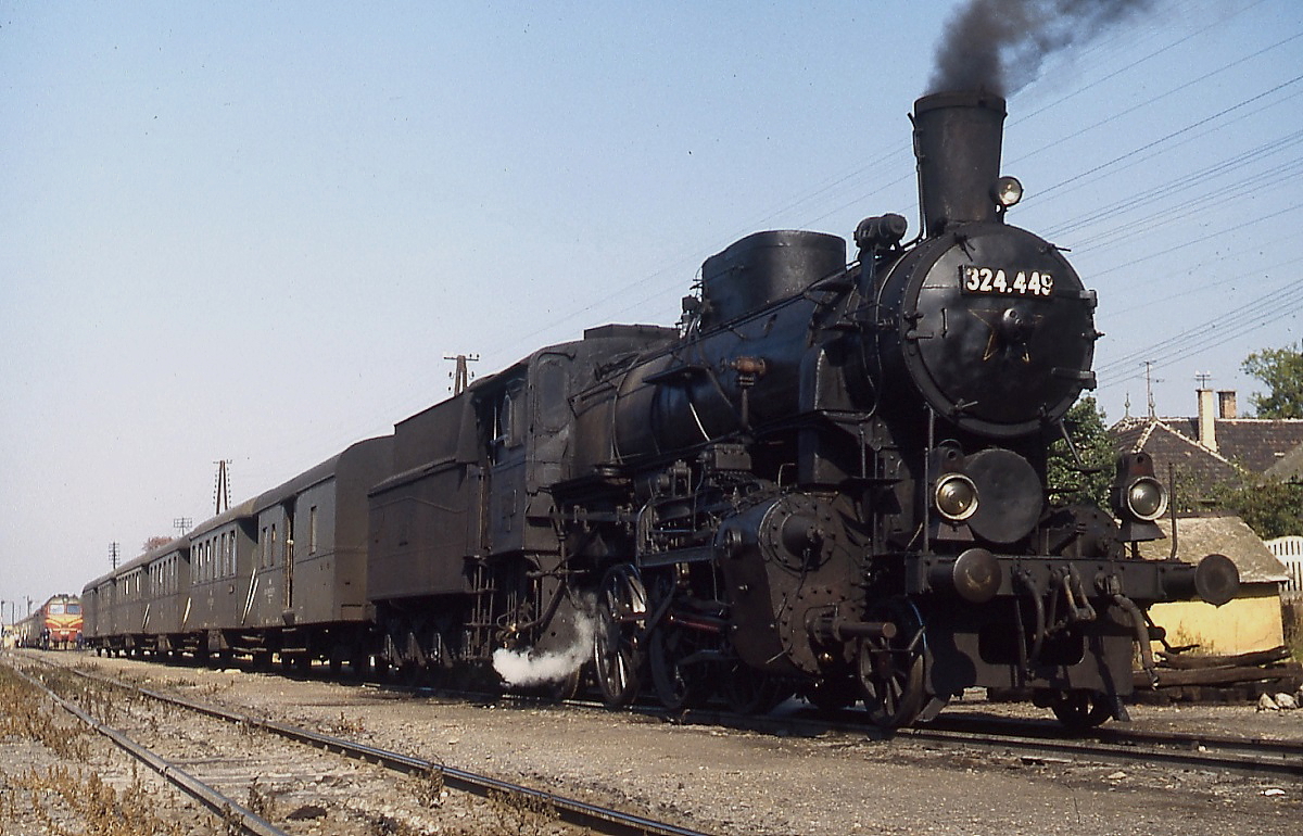 Auch die 1'C1'-Lokomotiven der Reihe 324, die zwischen 1909 und 1923 in Dienst gestellt wurden, waren im Oktober 1978 noch vereinzelt im aktiven Dienst anzutreffen. Die wenigen Güter- und Personenzüge der Strecke von Papa nach Tatabanya wurden komplett von dieser Reihe befördert. 324.449 wartet im Bahnhof Kisber mit einem klassischen Personenzug auf die Weiterfahrt nach Tatabanya.