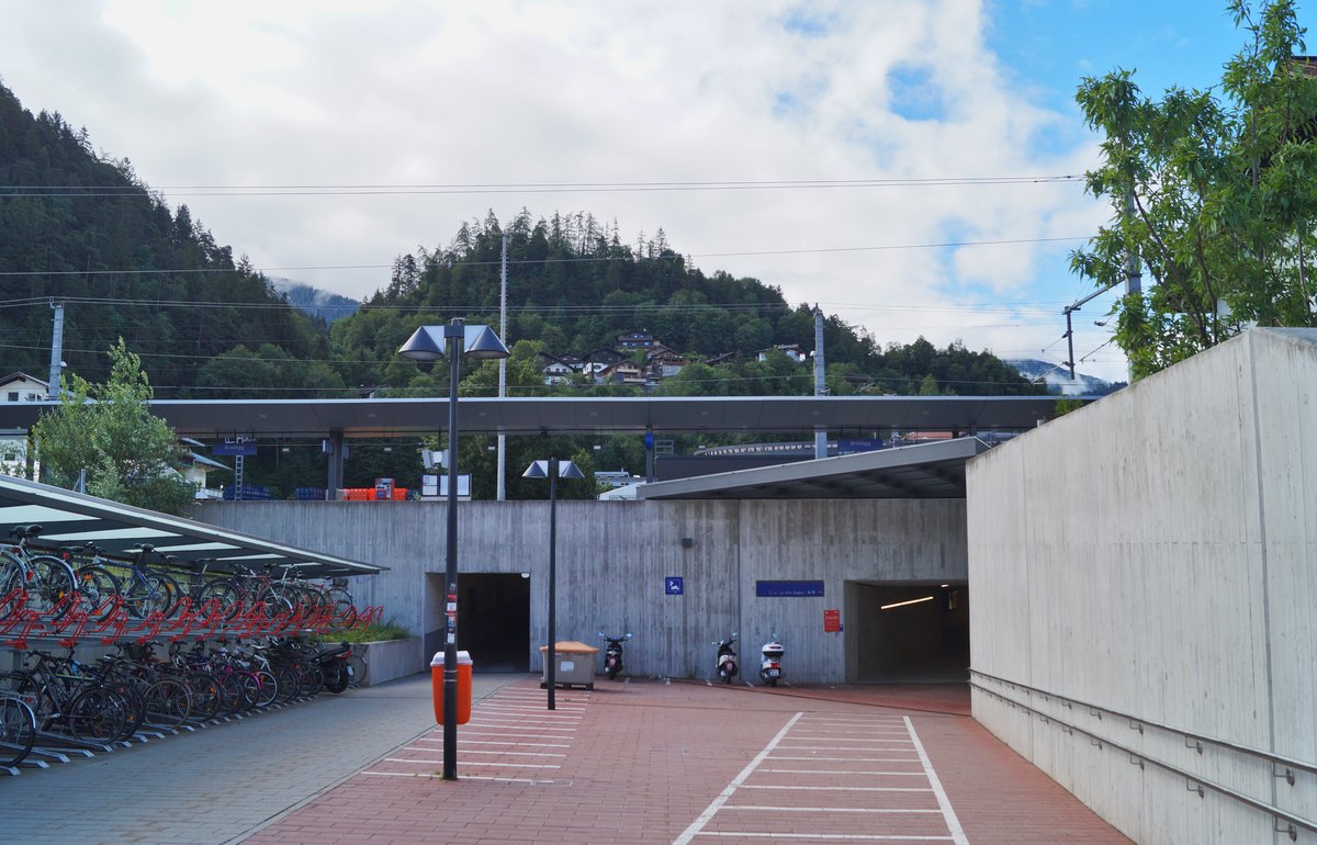 Auch der Bahnhof Brixlegg wurde im Zuge der sogenannten  Bahnhofsoffensive  modern umgebaut. Zentrales Merkmal dieser Umgestaltung ist die großflächige Verwendung von Beton. Blick auf die Abstellplätze für Fahrräder und Motorräder sowie den rückseitigen Bahnsteigzugang am 11.6.2020. Oben verläuft die Bahntrasse. 