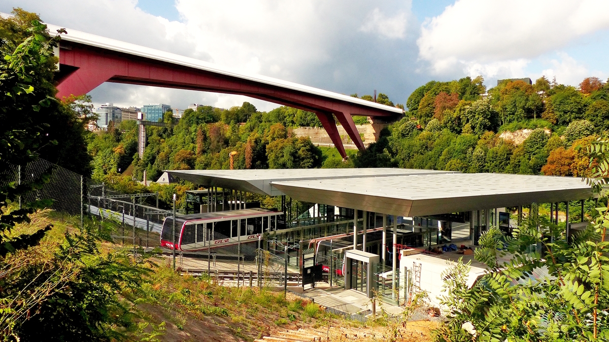 Auch wenn die Bume schon ihre herbstlichen Farben tragen, so wurde das Bild doch mitten im Sommer aufgenommen. Am 10.08.2018 verlsst ein Wagen der Standseilbahn Pfaffenthal-Kirchberg die Talstation, um die Fahrgste auf krzestem Weg nach Luxembourg-Kirchberg zur Tramhaltestelle Rout Brck-Pafendall zu befrdern. (Jeanny)