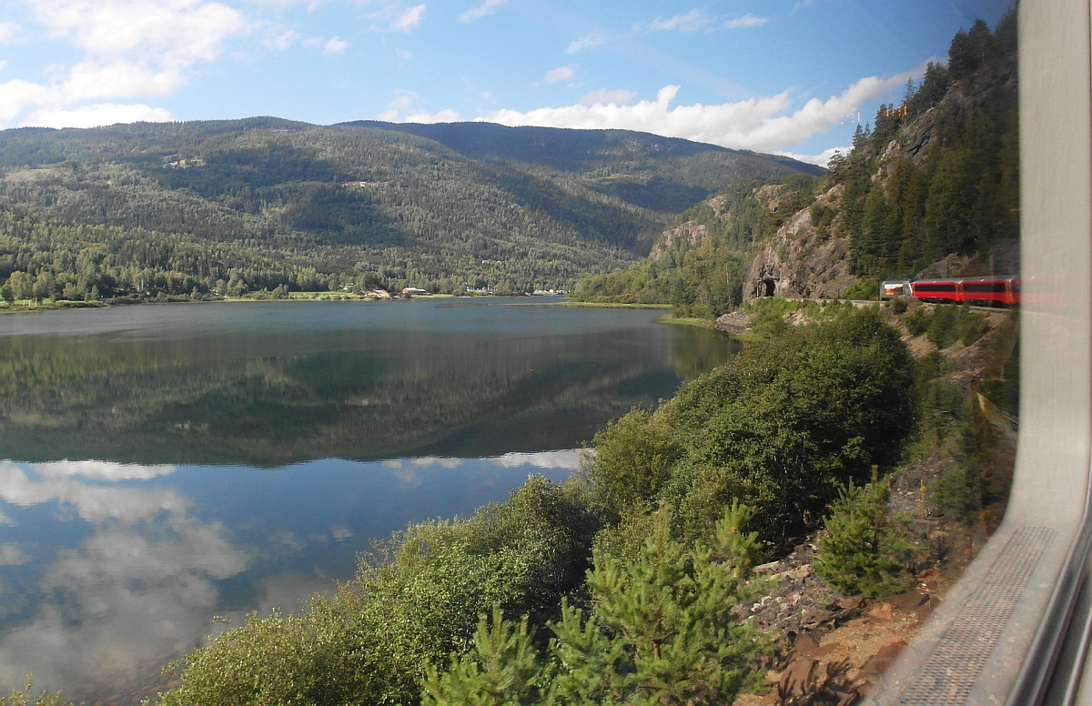 Auf der 471 km langen Strecke der Bergenbahn befindet sich der in Oslo gestartete und von El 18 2261 gezogene Zug Nr. 61 auf der Fahrt nach Bergen kurz vor Nesbyen. Am 20.08.2015 wurde aus dem vorletzten Wagen auf den Auslöser gedrückt, als der Zug am Fluss Hallingdalselva entlangfährt, der hier einige seiner breitesten Passagen hat.