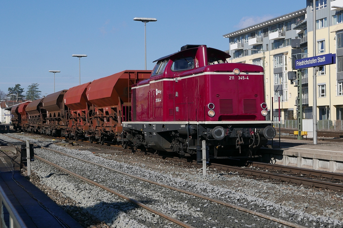 Auf den Einsatz wartend steht 211 345-4 der AIXrail mit mehreren Schotterwagen am 10.03.2017 auf Gleis 2 des Friedrichshafener Stadtbahnhofes.