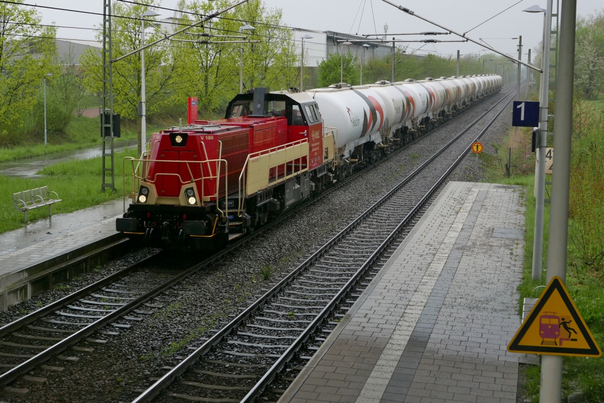 Auf der Fahrt von Gammertingen nach Konstanz passiert die V 180 der HzL, eine Gravita 15L BB, mit Holcim-Zementwagen am 16.04.2016 bei regenerischem Wetter die Haltestelle Konstanz Fürstenberg.