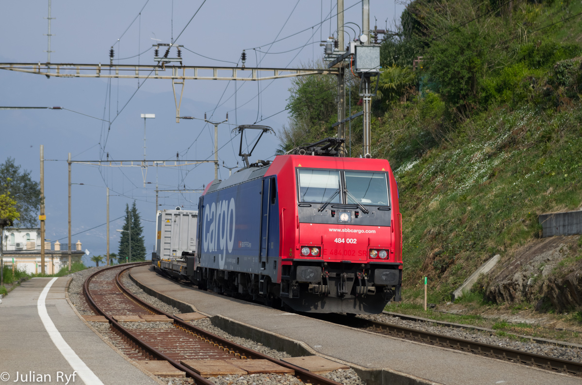 Auf der Linie Bellinzona-Luino(-Gallarate) sind die Güterzüge von SBB Cargo heute fast ausschliesslich mit modernen Loks aus der TRAXX oder EuroSprinter Familie bespannt. Neben den Re 474 kommen wie hier auch Re 484 zum Einsatz. Der Lokwechsel findet in diesen Fällen meistens in Bellinzona statt. Hier durchfährt Re 484 002 am 10. April 2015 gerade den Bahnhof San Nazzaro.