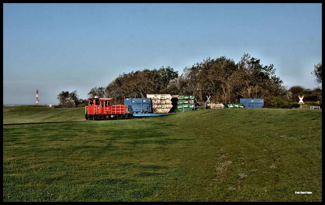 Auf Wangerooge wird der Müll, Bauschutt und sonstiger Abfall getrennt gesammelt und mit dem Zug vom Müll Sammel Platz abgeholt und zum Hafen gebracht. Am 1.10.2017 konnte ich einen solchen Transport im Bild fest halten. Lok Schöma 399108 hat beladene Müllcontainer vom Sammelplatz geholt und fährt über das Verbindungsgleis durch ein Deichtor zur Hauptstrecke.