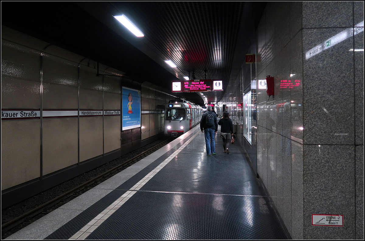 Auf zwei Ebenen unter Düsseldorf-Oberbilk -

1993 wurde die Tunnelstrecke vom Düsseldorfer Hauptbahnhof zur oberirdischen Station Ronsdorfer Straße mit zwei U-Bahnhöfen eröffnet. Daran schließt die Straßenbahnstrecke nach Düsseldorf-Eller als Zulaufstrecke an.

Das Bild zeigt die obere Ebene des doppelstöckigen U-Bahnhofes Handelszentrum/Moskauer Straße. Die beiden Bahnsteigebenen ergaben sich aus der Nähe des unterirdischen Überwerfungsbauwerkes der Strecken in Richtung Eller und in Richtung Holthausen. Dabei unterfährt das Gleis Richtung Eller die beiden Gleise von und aus Richtung Holthausen. 

Die Tunnelanlagen zwischen Hauptbahnhof und dem Bereich dieser Station sind sehr ausgedehnt und komplex. Zwischen den beiden U-Bahnhöfen liegen ganze acht Gleise nebeneinander, jeweils außen zwei Streckengleise und innen vier Abstell- bzw. Wendegleise. 
Obwohl es nur zwei Bahnsteiggleise gibt liegen auch im Bereich der Haltestelle Handelszentrum/Moskauer Straße drei Gleise. Diese dritte Gleis zweigt von von der Innenstadt her kommend vor dieser Station nach rechts vom Streckengleis ab und steigt neben der unteren Bahnsteigebene auf die Höhe des oberen Gleise an, da dirkt östlich der Station sich eine weitere zweigleisige Wendeanlage auf der Südseite der Streckengleise  befindet. Dessen Gleis in Fahrtrichtung Innenstadt überfährt das tieferliegende Streckengleis und mündet vor dem oberen Bahnsteig wieder in das Streckengleis Richtung Hauptbahnhof. Hier endende Kurse müssen ihre Fahrgäste schon am Hbf aussteigen lassen, während in die hier beginnenden Linien schon am Handelszentrum eingestiegen werden kann.

Bei Openstreetmap kann man die Gleisführungen nachvollziehen. 
Übrigens wurde die Wehrhahnlinie weit einfacher ausgeführt, ein durchgehend zweigleisiger Tunnel, ohne Abzweige, Wendegleise und Abstellanlagen.

14.10.2019 (M)