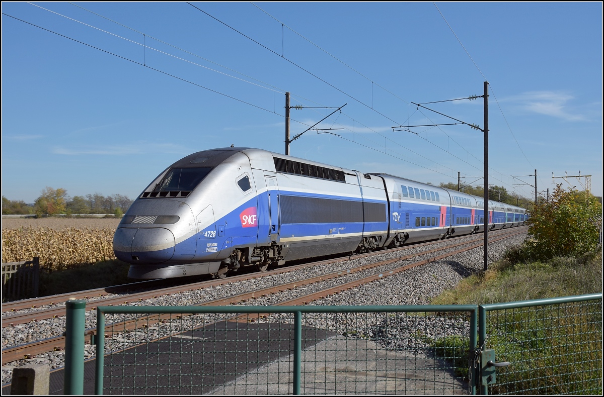 Bahn im südlichen Elsass. TGV Duplex 4726 mit Triebkopf 310 054 voraus fährt Richtung Paris am Flughafen Basel/Mühlhausen vorbei, recht sieht man noch die Befeuerung des Landeanflugs, unmittelbar dahinter beginnt die Landebahn des Flughafens. Bartenheim, Oktober 2017.