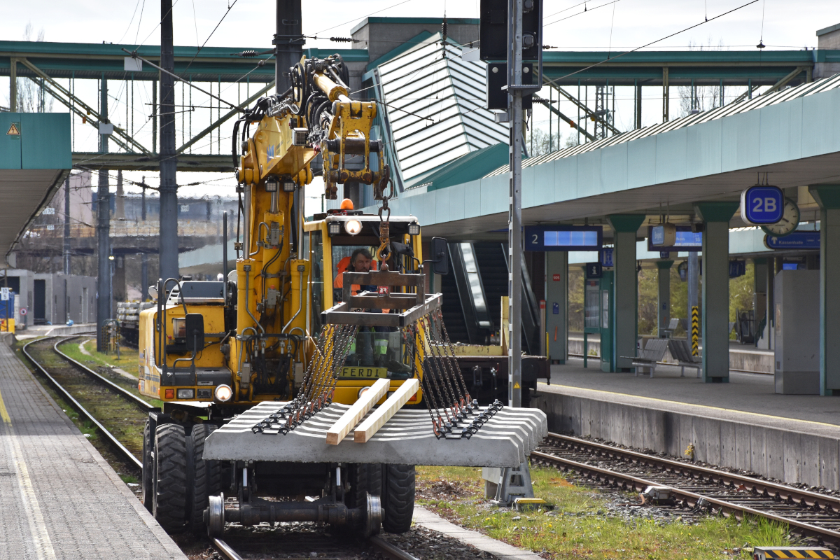 Bahnbau in Vorarlberg: Die ÖBB nutzen die Streckensperre im Zuge der Bauarbeiten zwischen Lauterach und Hard, um gleichzeitig auch im Bahnhof Bregenz die nicht mehr zeitgemäßen Holzschwellen durch Betonschwellen zu ersetzen (als erster Schritt in Richtung Bahnhofsneubau). Ein Liebherr Zweiwegebagger der Bahnbau Wels GmbH transportiert am 09.04.2021 ein neues Schwellenelement. Trotz der Bauarbeiten blieb der Bahnsteig frei benutzbar.