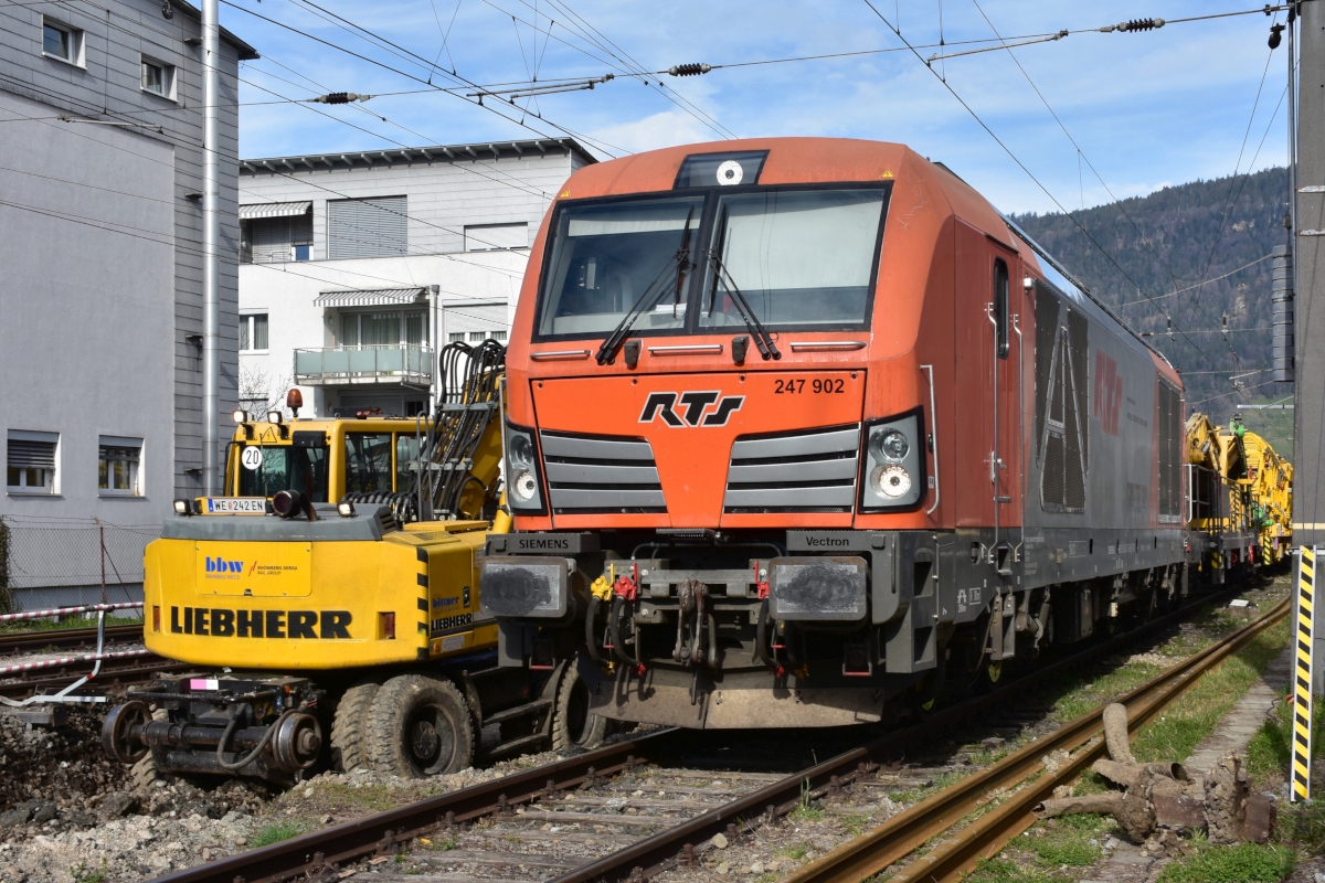 Bahnbau in Vorarlberg: Die ÖBB nutzen die Streckensperre im Zuge der Bauarbeiten zwischen Lauterach und Hard, um gleichzeitig auch im Bahnhof Bregenz die nicht mehr zeitgemäßen Holzschwellen durch Betonschwellen zu ersetzen (als erster Schritt in Richtung Bahnhofsneubau). Obwohl die Rail Transport Service GmbH (RTS) ein österreichisches Unternehmen ist (es steht auch die Grazer Adresse auf der Lok), wurde die Diesel-Vectron 247 902 in Deutschland registriert (92 80 1247 902-0 D-RTS). Neben der Lok steht am 09.04.2021 ein Liebherr-Zweiwegebagger der Bahnbau Wels an der West-Einfahrt in den Bahnhof Bregenz. Fotostandort: am öffentlichen Weg, über den Zaun fotografiert. 