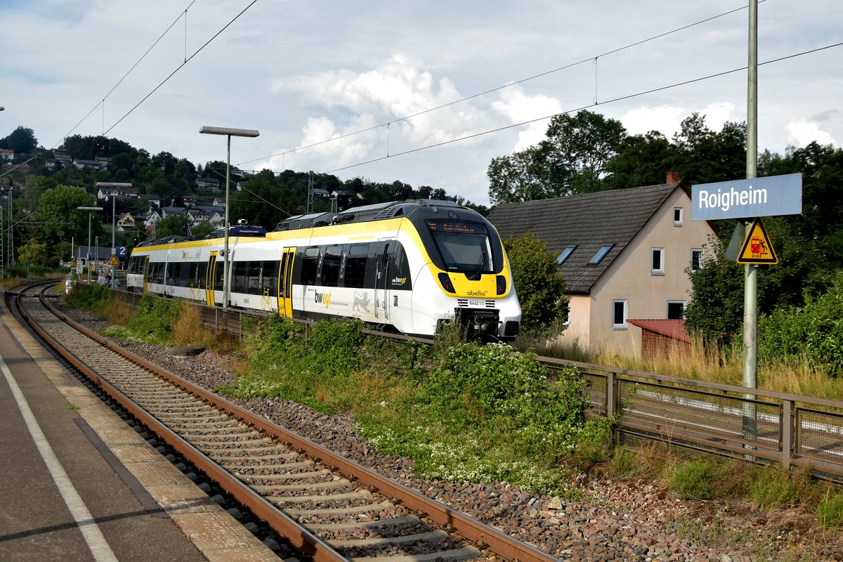 Bahnhofsschild des Bahnhof Roigheim an der Frankenwaldbahn.
Aufgenommen am 17.8.2020. Im Hintergrund ist ein Abelliotriebwagen als RB 18 nach Osterburken zu sehen.