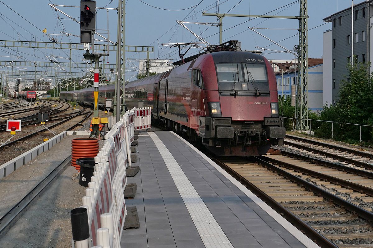 Bahnsteigerneuerung und Bahnbetrieb (|) - Am zweiten, bereits erneuerten Bahnsteig von insgesamt fünf zu erneuernden Bahnsteigen zieht 1116 154 die Wagen des RJ 890, Bregenz - Frankfurt (M), am 10.07.2023 in den Friedrichshafener Stadtbahnhof
