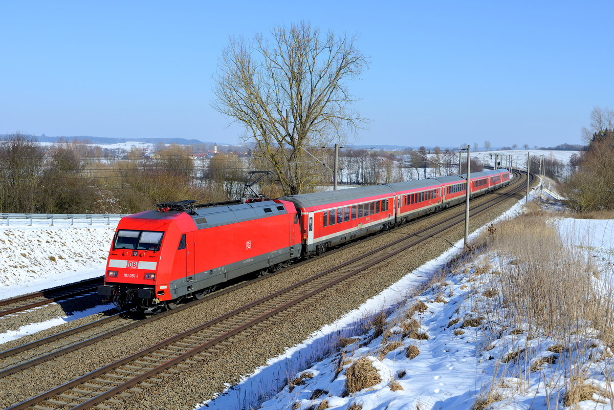 Bald steht die Ablöse an: Am 24. Februar 2018 verkehrte der München-Nürnberg-Express noch in der klassischen Reihung mit einer Lok der Baureihe 101 von DB Fernverkehr und dem Wendezug, bestehend aus ehemaligen IC-Wagen. Doch noch in diesen Jahr wird der Wechsel auf Doppelstockwagen und Loks der Baureihe 102 vollzogen. An diesem klirrend kalten Tag zeigte sich das Dachauer Hinterland mit einer geschlossenen Schneedecke. Die frisch revisionierte 101 051 setzte mit ihrer kräftig leuchtenden verkehrsroten Lackierung einen Akzent in der winterlichen Landschaft bei Vierkirchen.